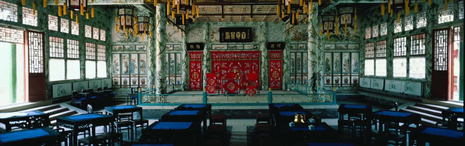 画面展示了一间装饰华丽的中式古建筑室内，中央有红色雕饰屏风，周围摆放着木桌椅。
