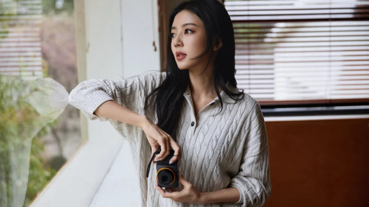 一名女性站在窗边，手持相机并望向一侧。