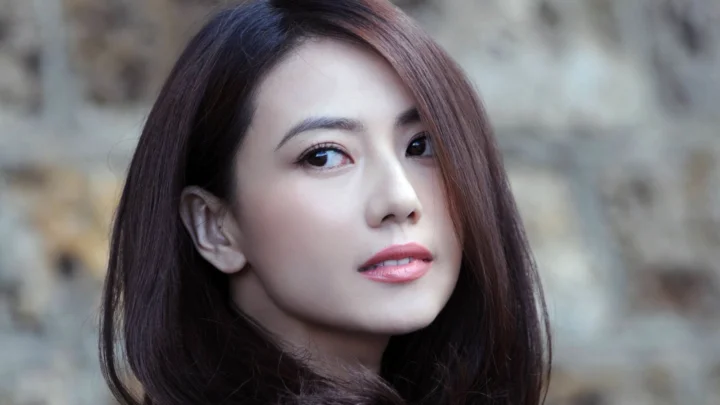 흐릿한 배경을 뒤로한 갈색 긴 머리 여성의 클로즈업 인물 사진입니다.