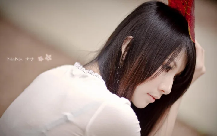 一名长发女子穿着白色上衣侧身靠坐，低头望向画面右侧。