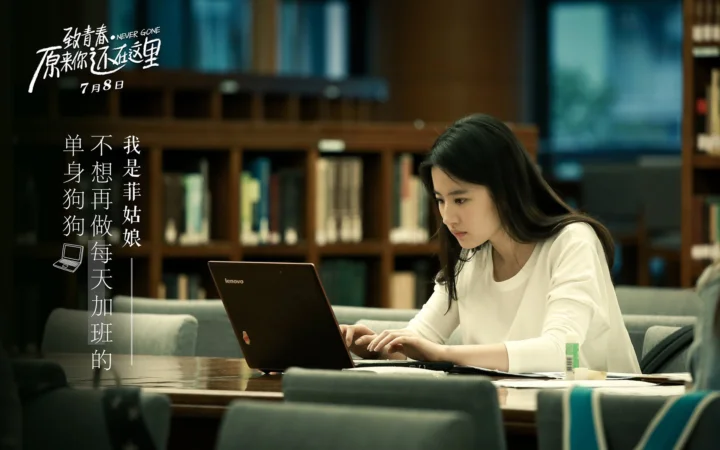 一名女子坐在桌前使用笔记本电脑，身后是书架和室内座椅。