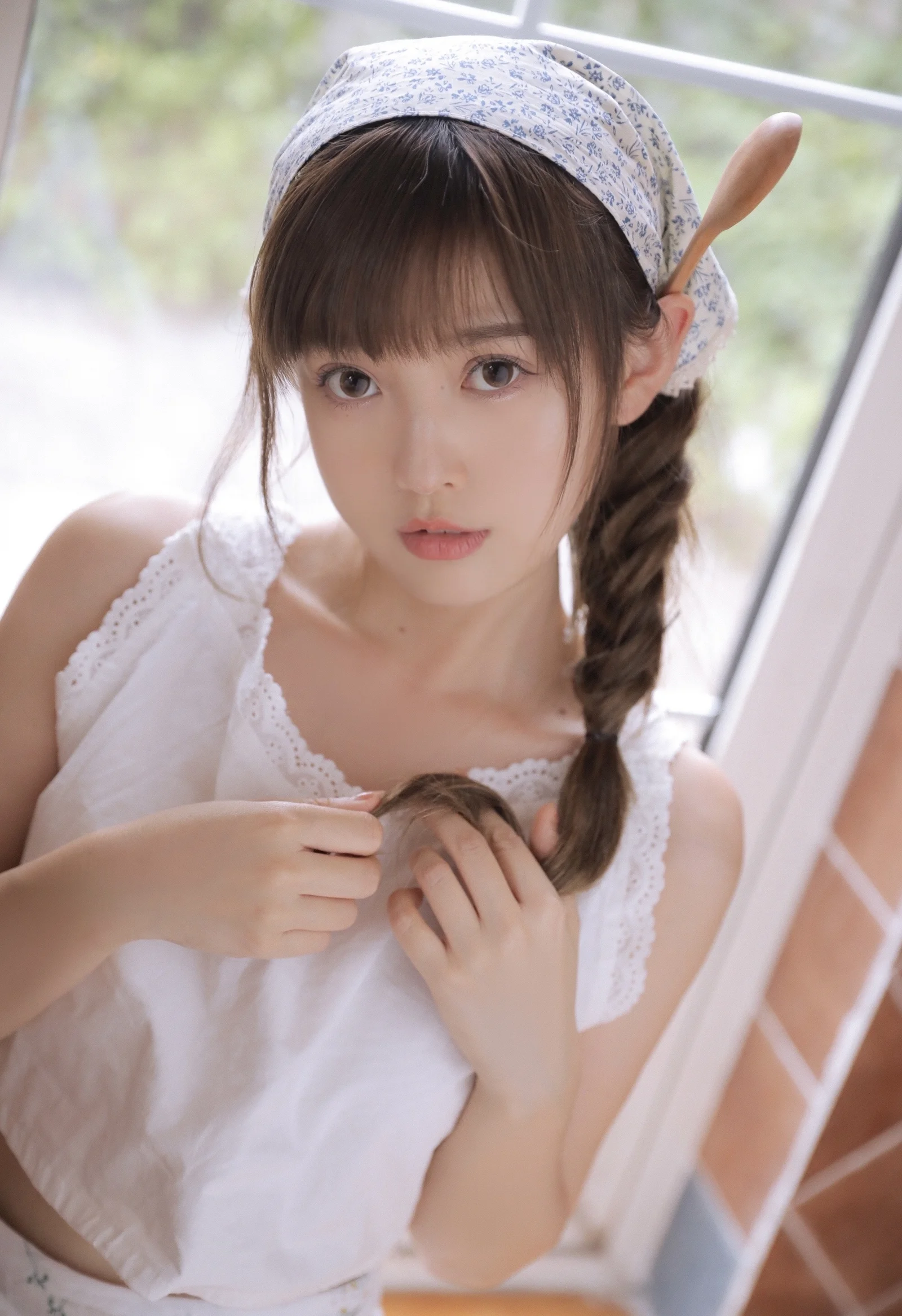 一位戴着花纹头巾、留着长辫子的女性站在窗边看向镜头。