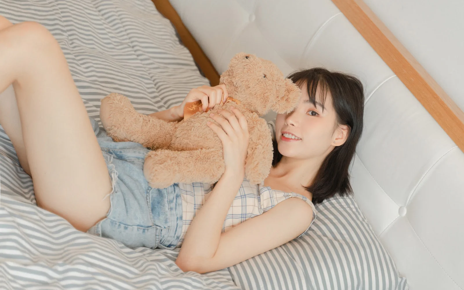 一名女子躺在床上抱着一只棕色泰迪熊。
