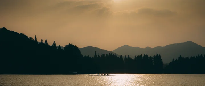 夕阳映照湖面，远处群山与森林呈现出宁静的剪影。