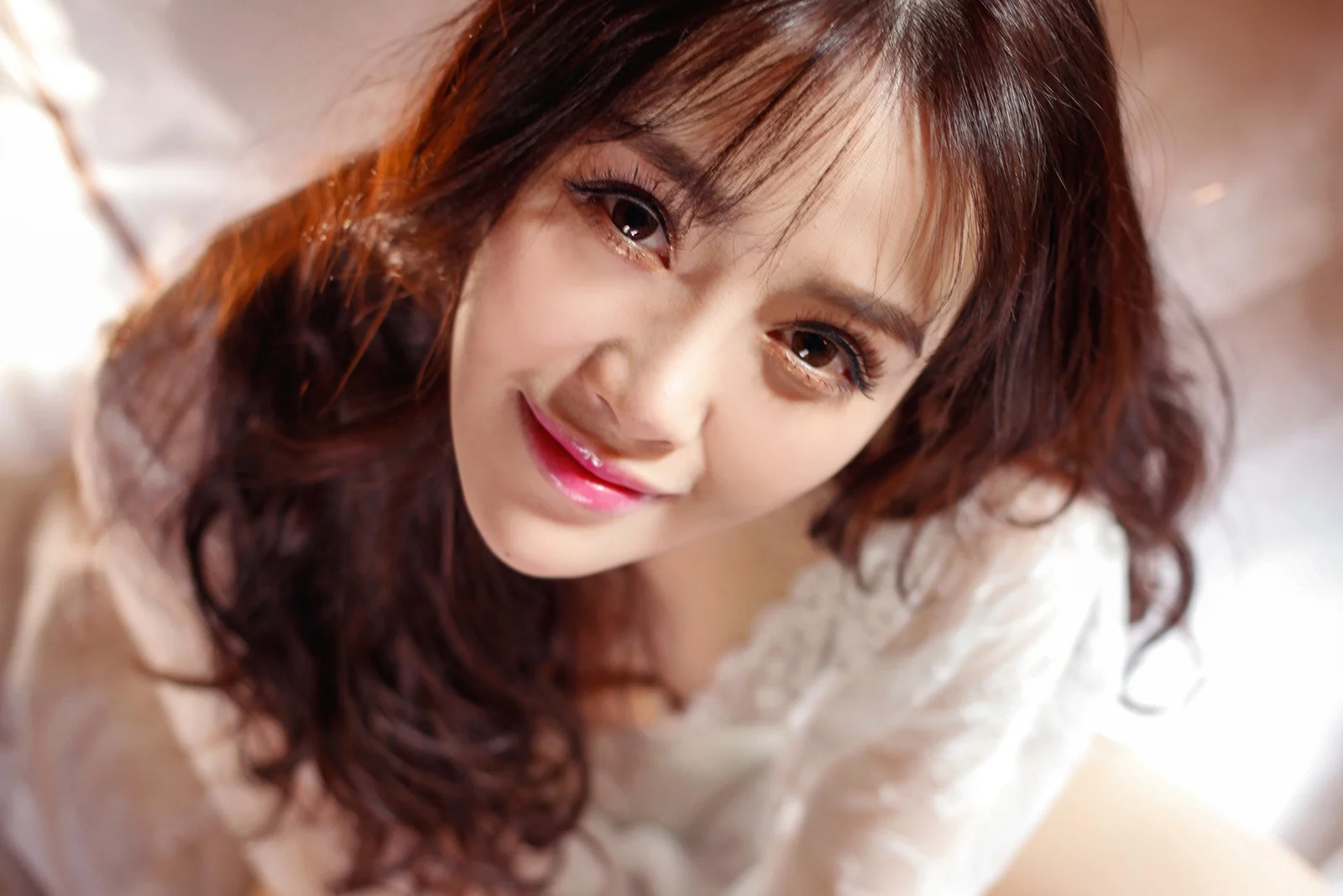 갈색 긴 머리의 여성이 흰색 상의를 입고 미소 짓는 근접 인물 사진입니다.