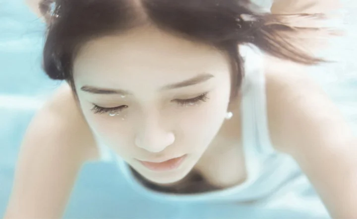 一名闭着眼睛的成年女性在水中低头，湿发散开，脸部和肩膀占据画面大部分。