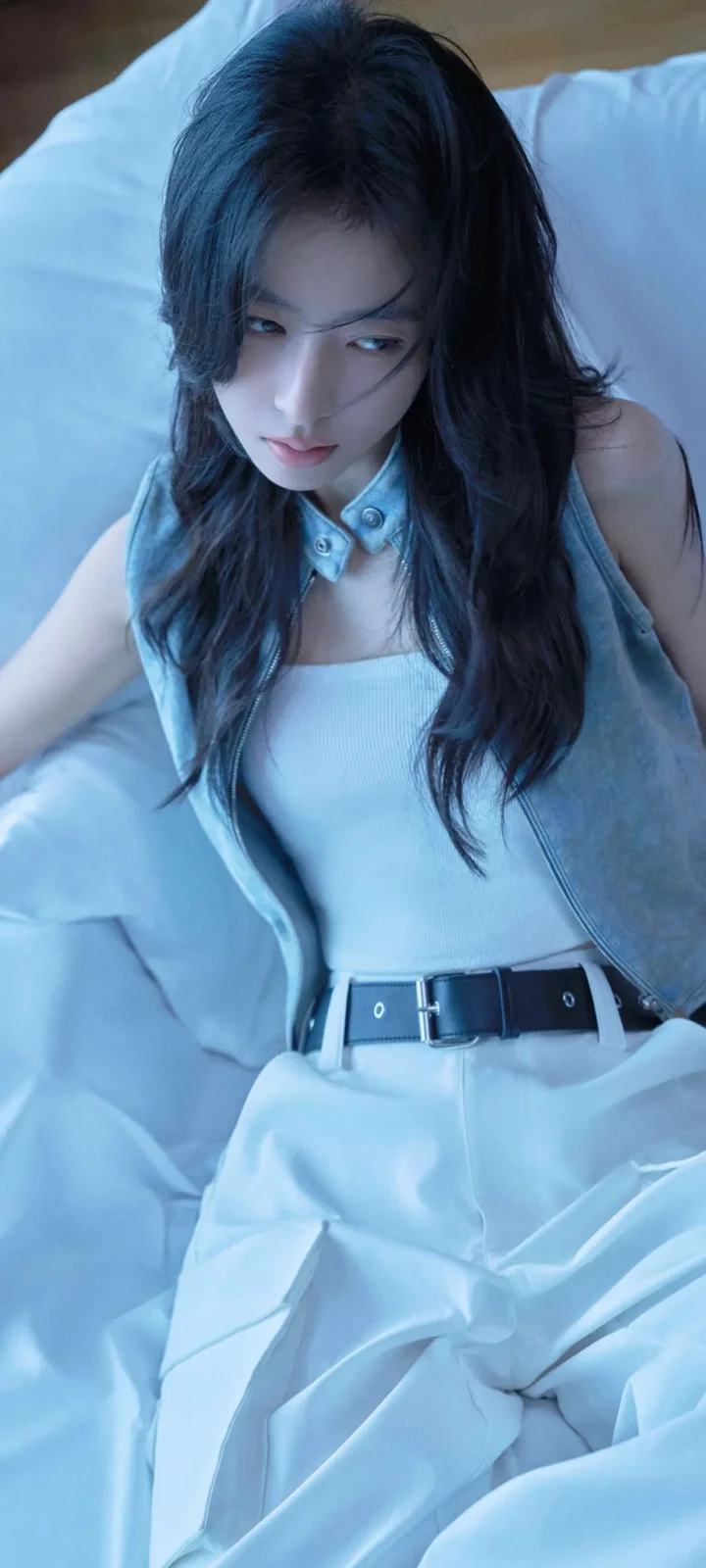 一名长发女性身穿浅色无袖服装坐在床上，整体画面呈现冷蓝色调。