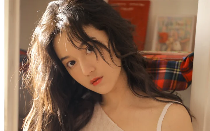 一位长发女性在室内阳光下侧头注视镜头。