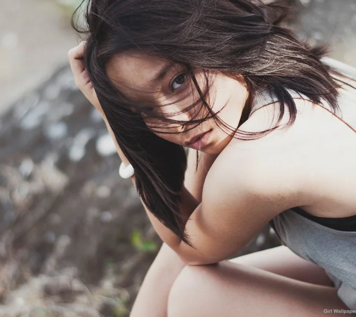 바람에 긴 머리를 흩날리며 야외에서 고개를 숙이고 있는 검은 머리 여성.