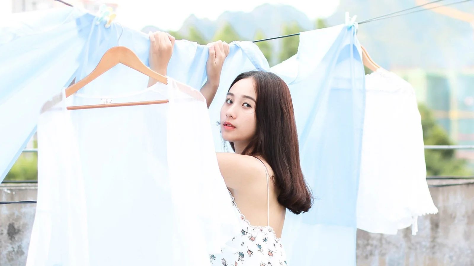 성인 여성이 야외에 널린 흰색 옷들 사이에서 뒤돌아 카메라를 바라보고 있다.