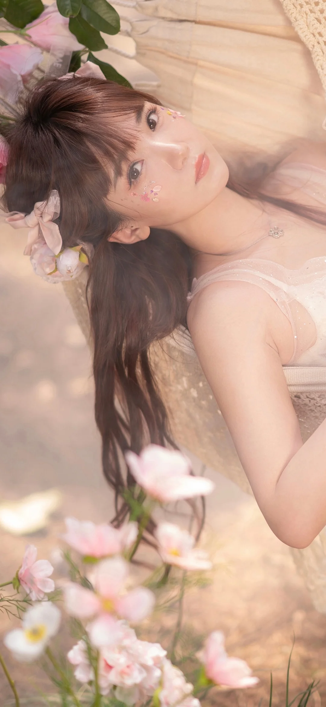 一位长发女子躺在柔和的粉色花朵间，画面呈现温柔朦胧的氛围。