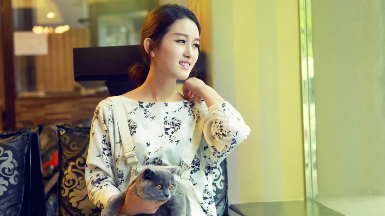 一名女子在室内窗边抱着一只灰猫。