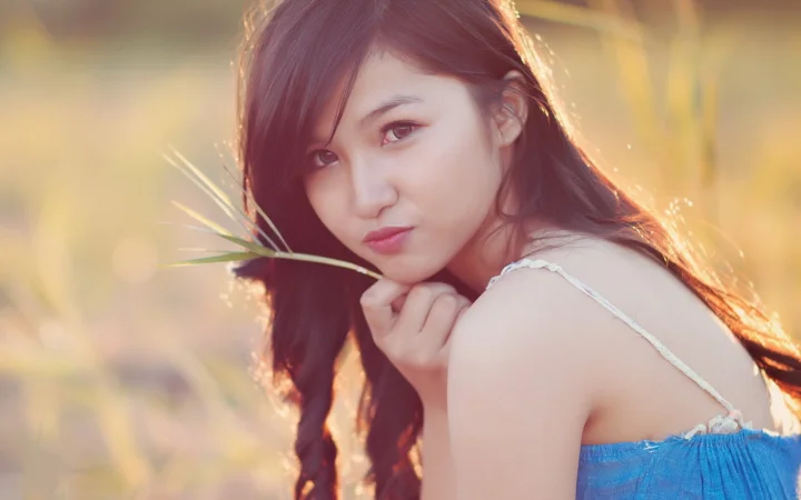 一位长发女性在温暖的户外光线下将一根草叶靠近脸庞。