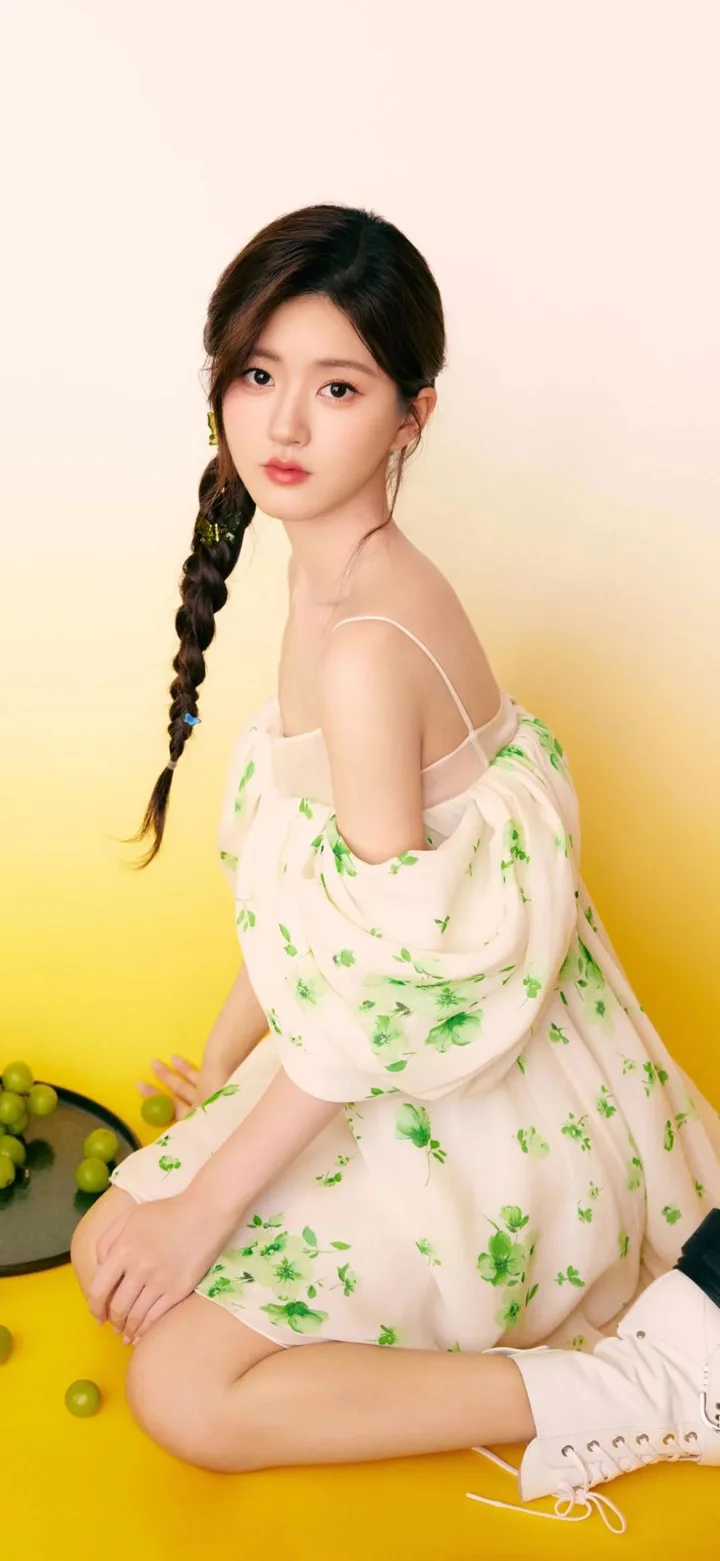 一名成年女性穿着浅色碎花裙，编着侧边长辫，坐在明亮的黄色背景前。