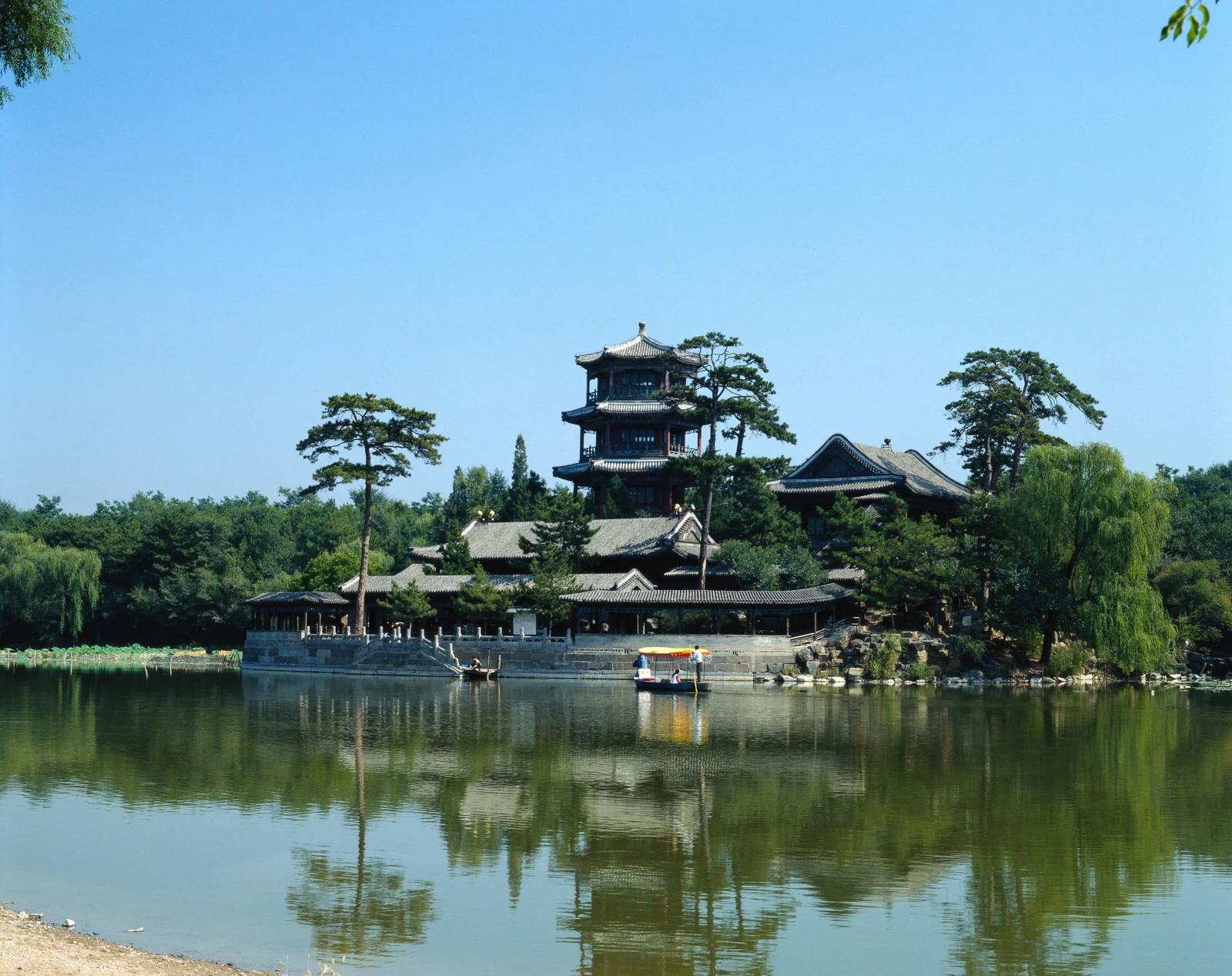 湖畔的中式古建筑群掩映在树木之间，倒映在宁静的水面上。