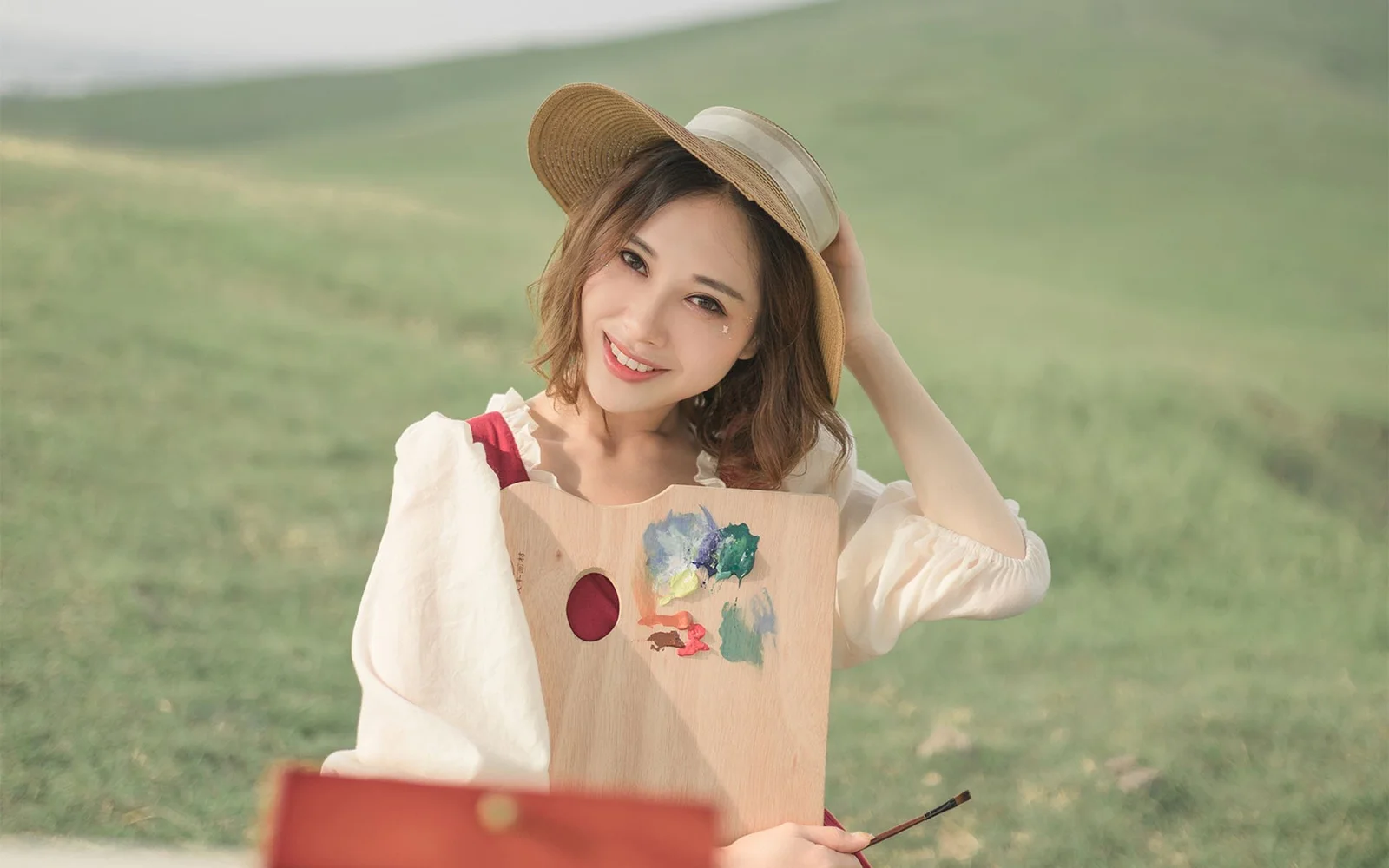 一名戴着宽檐帽的女性站在绿色草地前微笑。