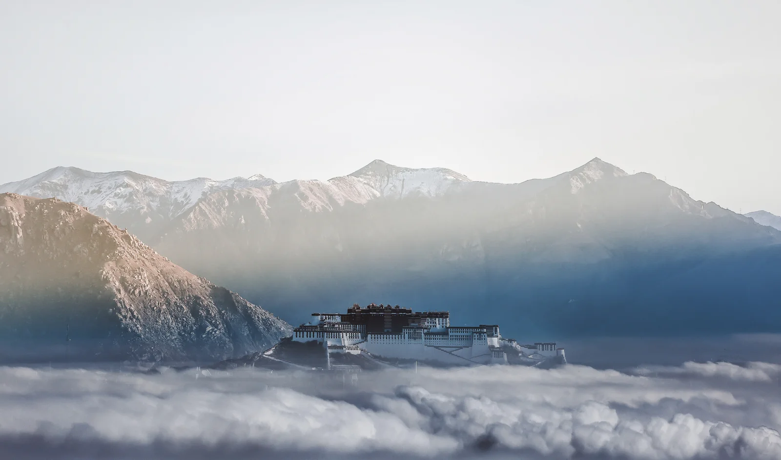 雪山が雲海と薄霧の上に連なり、遠くに高原の宮殿建築が見える。
