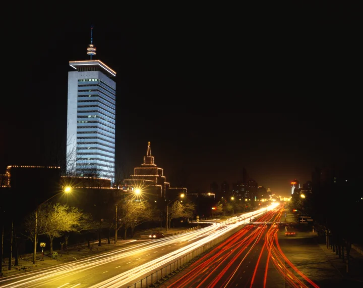 夜晚的城市道路延伸至远方，高楼、街灯和车辆形成明亮的光轨。