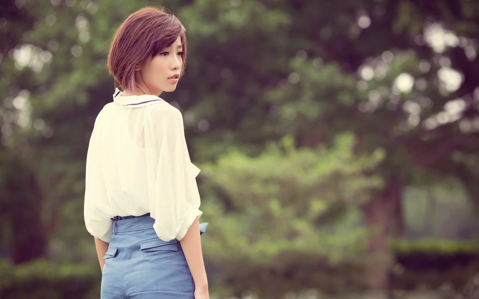 一位穿白色上衣的成年女性站在綠樹環繞的公園中回眸望向鏡頭。