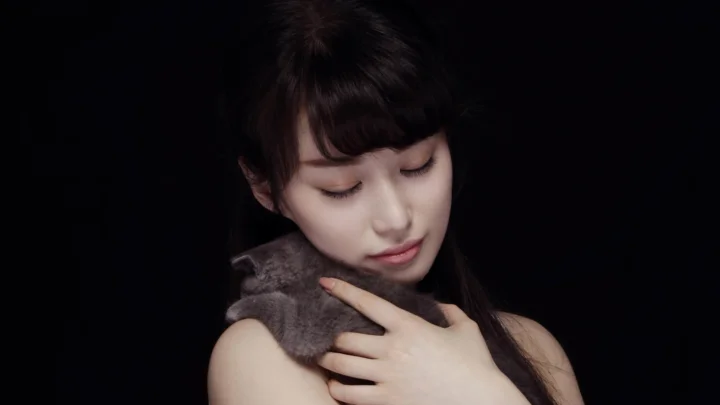 一名闭眼的女性在黑色背景前轻抚围在颈间的灰色围巾。