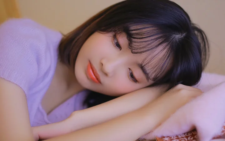 一名黑发女子身穿淡紫色上衣，侧头枕在手臂上。