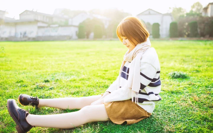 スカーフを身につけた女性が、明るい日差しの草地に座っている。