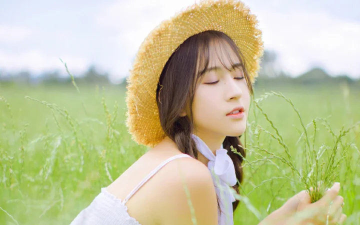 一名戴草帽的女子闭眼站在绿意盎然的草地中。