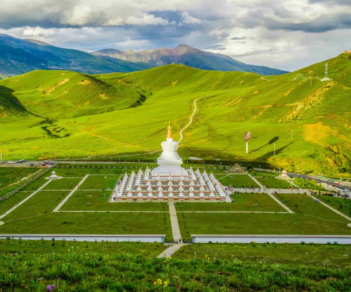 绿色山丘之间坐落着一座白色佛塔，远处群山笼罩在云层下。