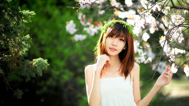 一名女子站在绿意盎然的树林和盛开的樱花枝下。