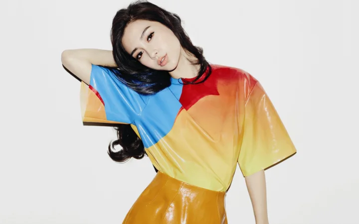 一名成年女性穿着彩色光泽上衣，在浅灰色背景前摆姿势。