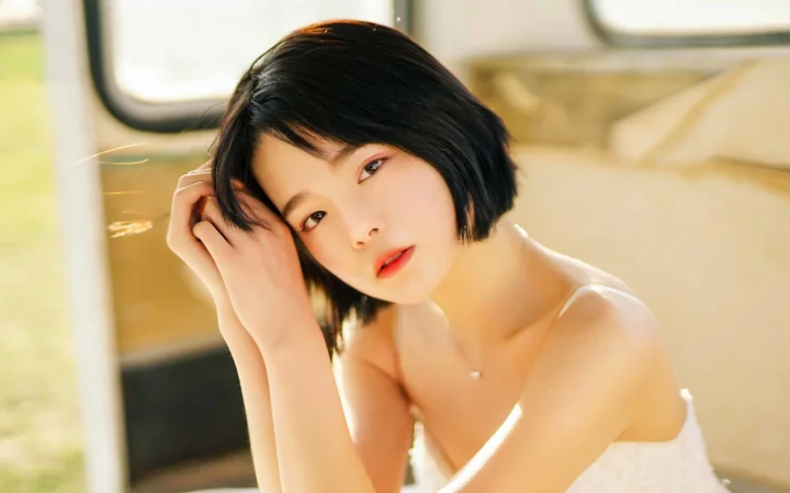 一位留着黑色短发的女性在暖色光线下靠近镜头整理头发。