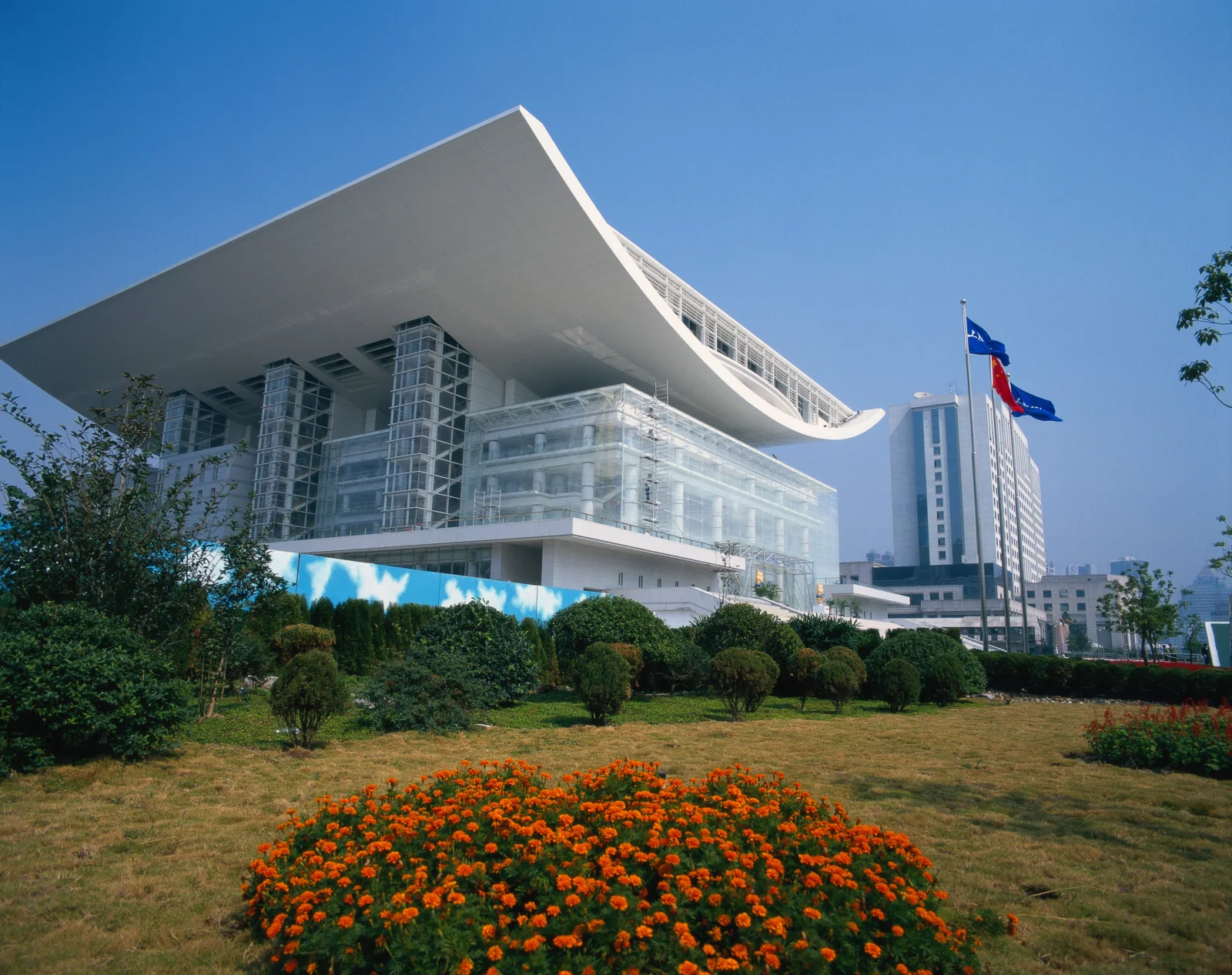 蓝天下，一座现代建筑矗立在修剪整齐的花园和橙色花坛之后。