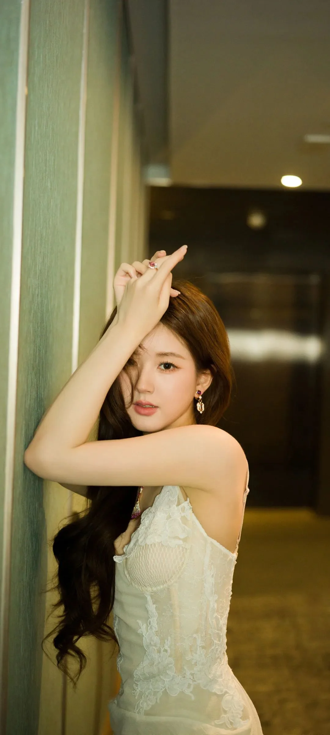 一名成年女性穿著白色蕾絲裙在室內牆邊擺姿勢。