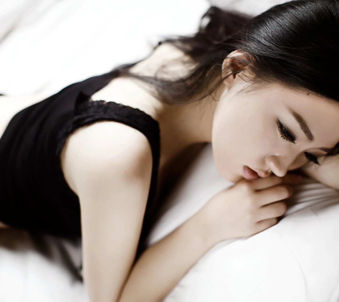 흰색 침대에 눈을 감고 옆으로 누워 쉬는 성인 여성.