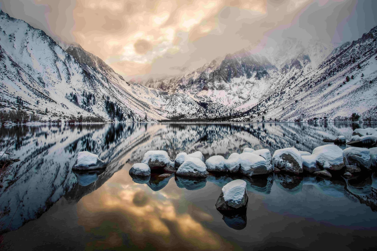 积雪覆盖的群山环绕着宁静湖泊，湖面倒映着天空、山峰和前景的积雪岩石。
