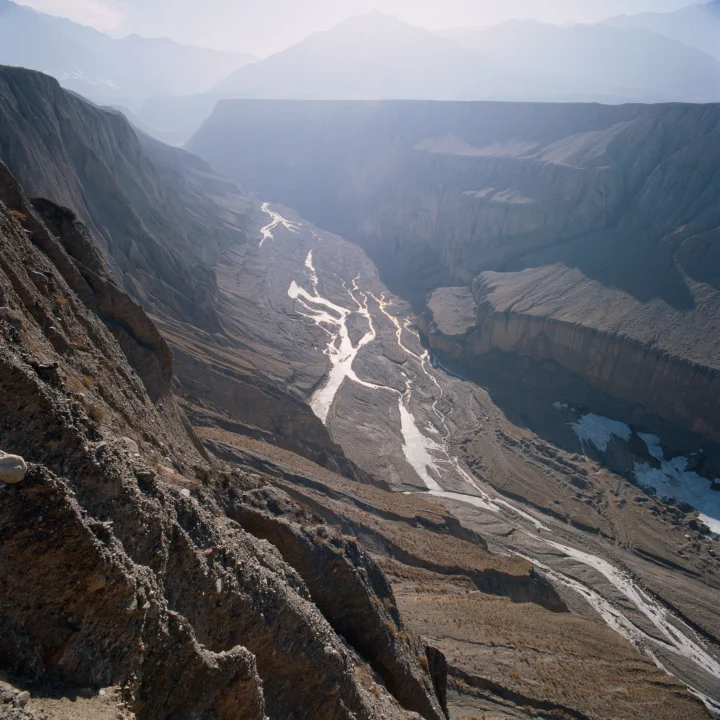 高山峡谷间，一条蜿蜒的冰川融水河流穿过荒凉的岩石地貌。