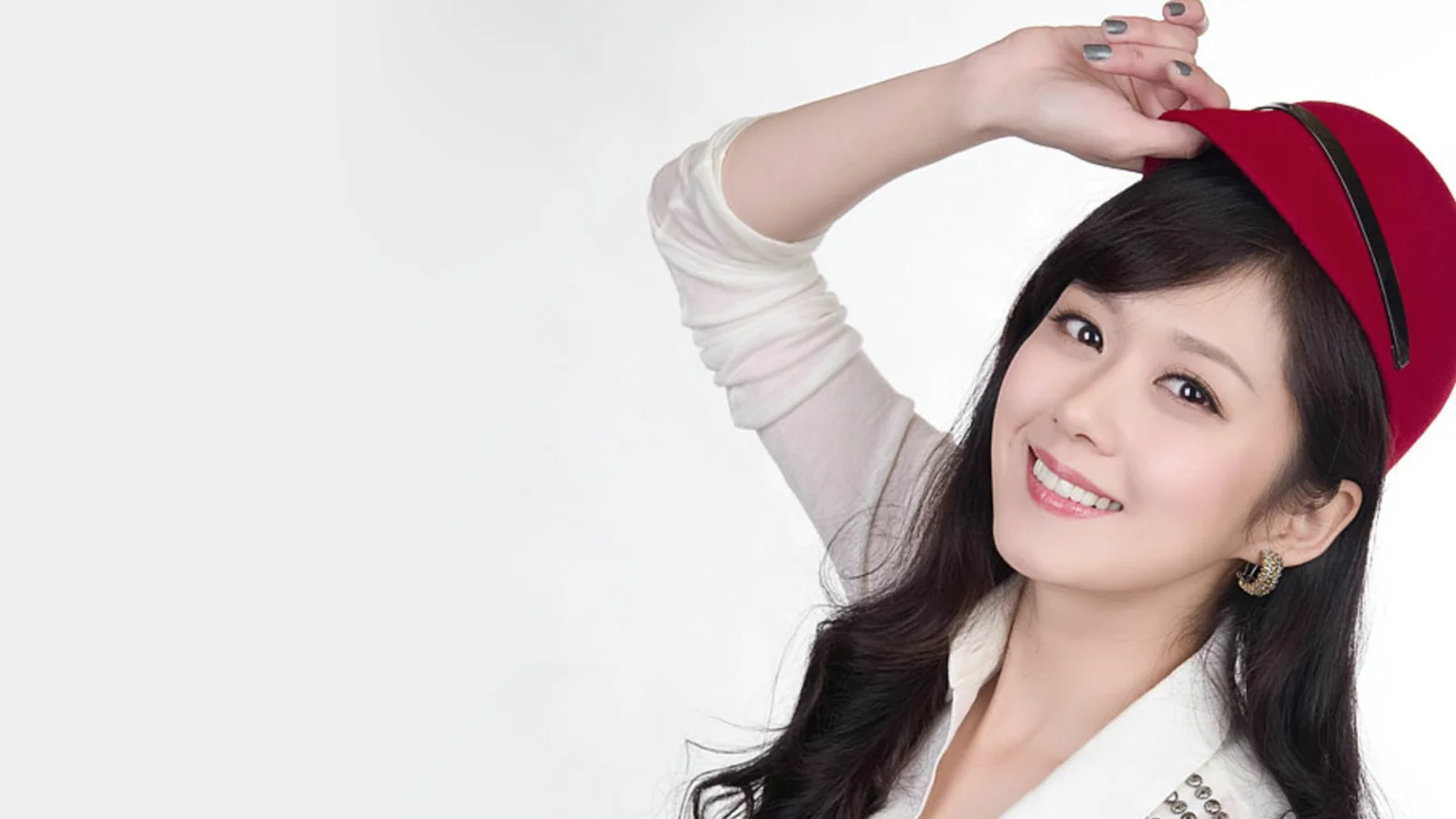 빨간 모자를 쓴 긴 머리 여성이 밝은 배경 앞에서 미소 지으며 포즈를 취하고 있습니다.