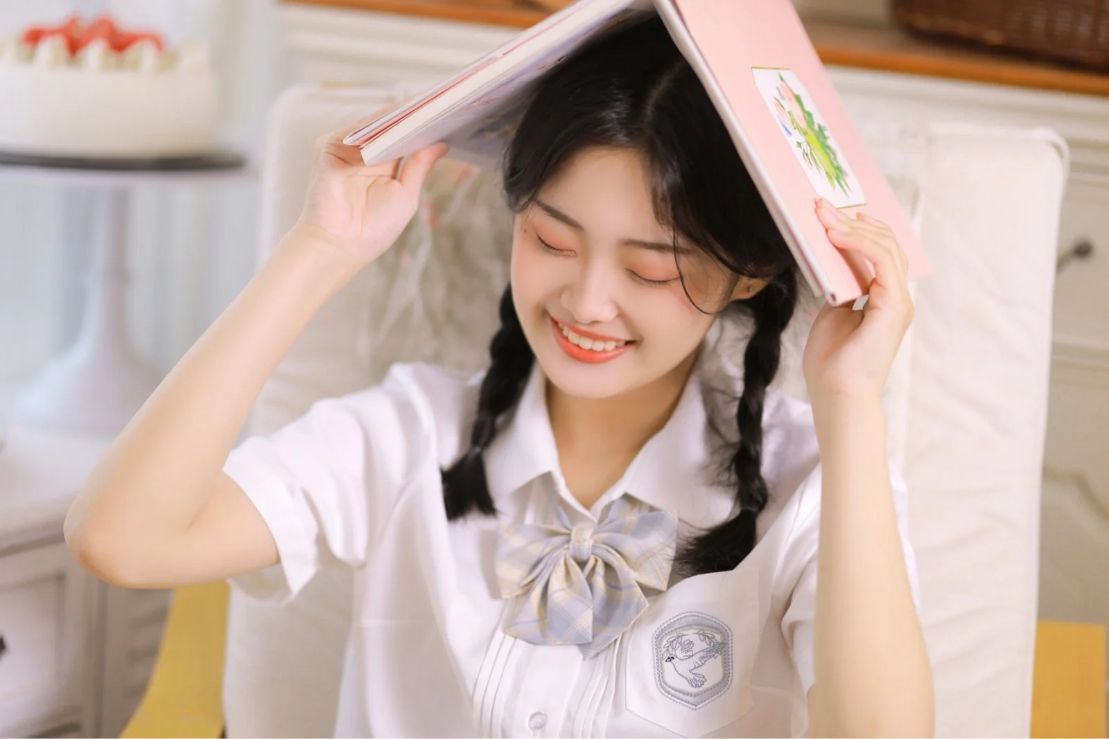 미소 짓는 여성이 실내에서 분홍색 책을 머리 위로 들고 있습니다.
