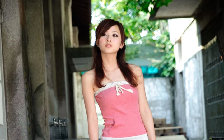 一名穿粉色连衣裙的女性站在绿荫映衬的狭窄通道中。