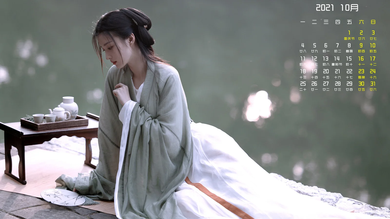 연한 색상의 전통 의상을 입은 여성이 흰 침구 옆에 앉아 있고, 곁에 다기가 놓여 있으며 오른쪽 위에 달력 글자가 겹쳐져 있습니다.