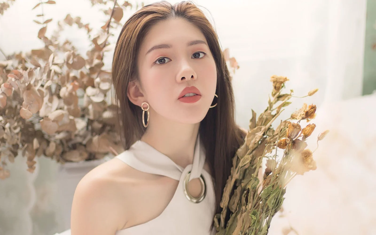 一位成年女性在室内手持干花束面对镜头。