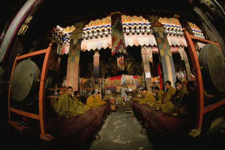 一座装饰华丽的寺庙内，僧人坐在中央祭坛两侧，入口处悬挂着大鼓。