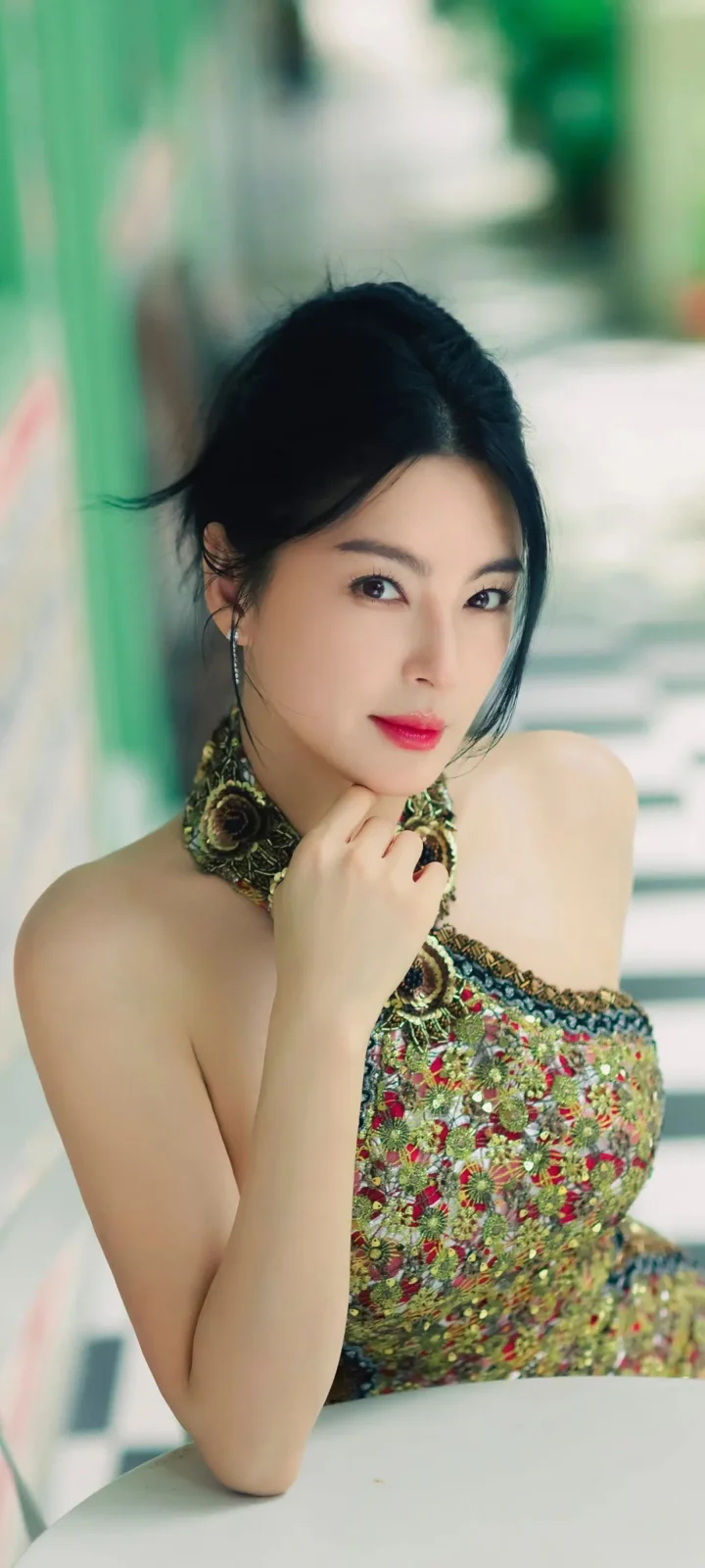 一位成年女性身穿彩色花纹礼服，在明亮背景前注视镜头。