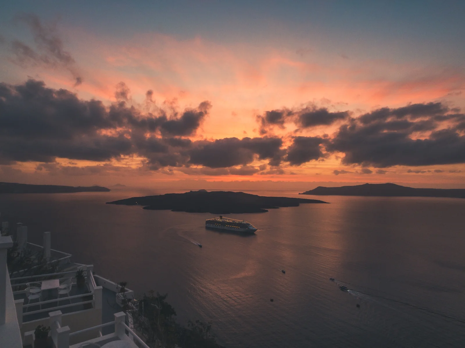 夕阳将天空染成橙粉色，映照着海面、远处岛屿和航行中的船只。