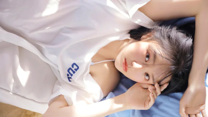 一名女子穿着白色上衣躺在蓝色织物上，阳光洒在她的脸庞和衣服上。