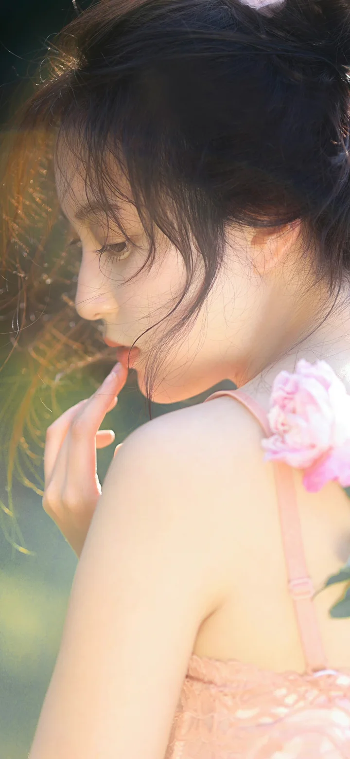 ピンクの服を着た女性が柔らかな日差しの中で振り返り、肩元にピンクの花を添えています。