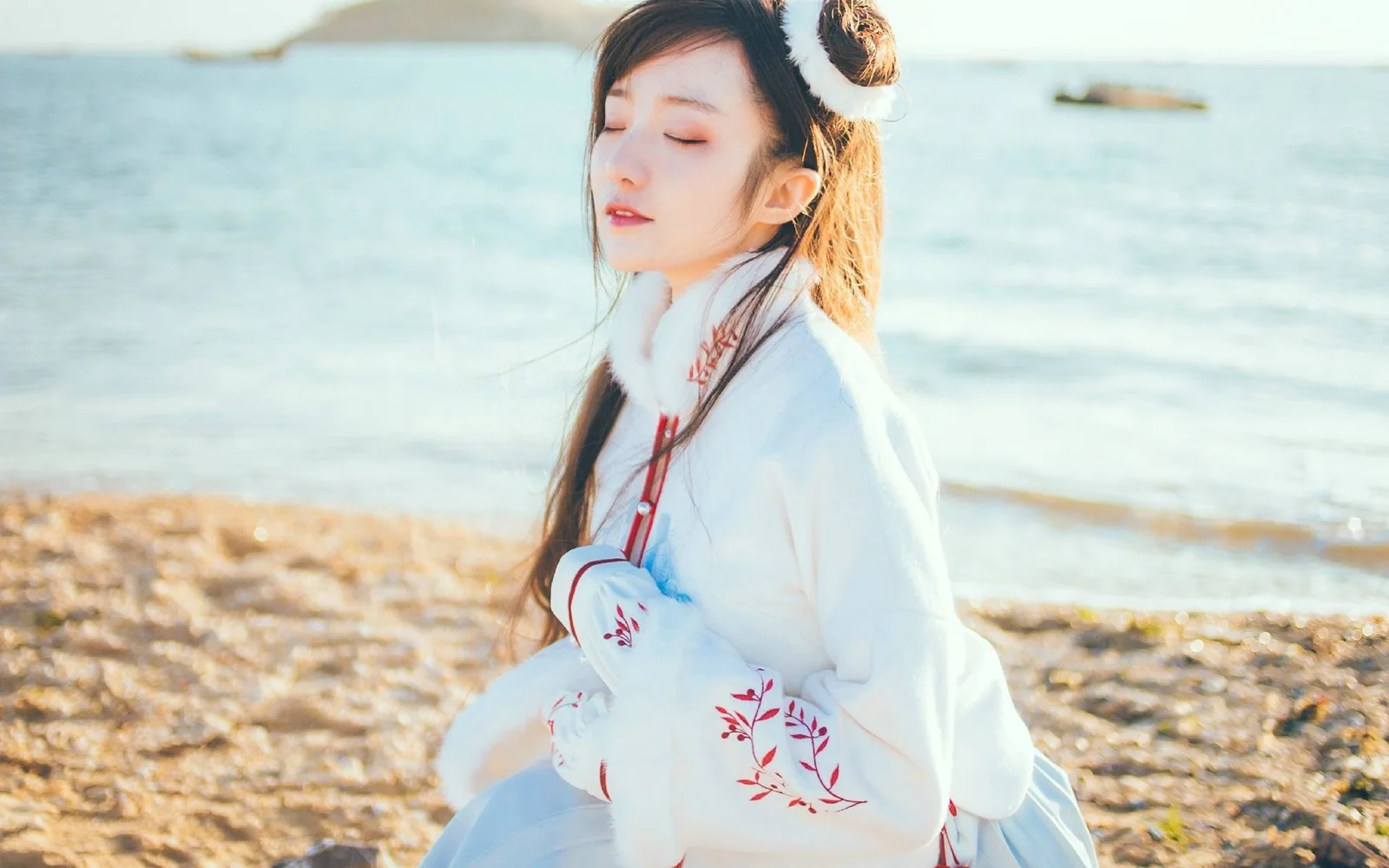 흰 옷을 입은 여성이 잔잔한 바다를 배경으로 해변에 앉아 있습니다.