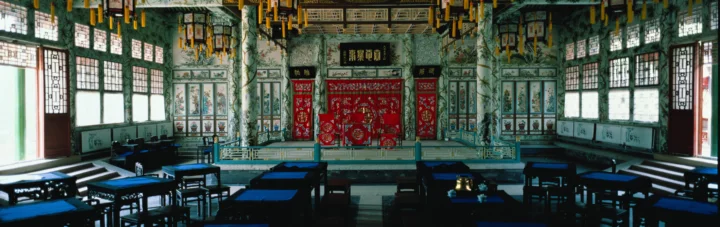 画面展示了一间装饰华丽的中式古建筑室内，中央有红色雕饰屏风，周围摆放着木桌椅。