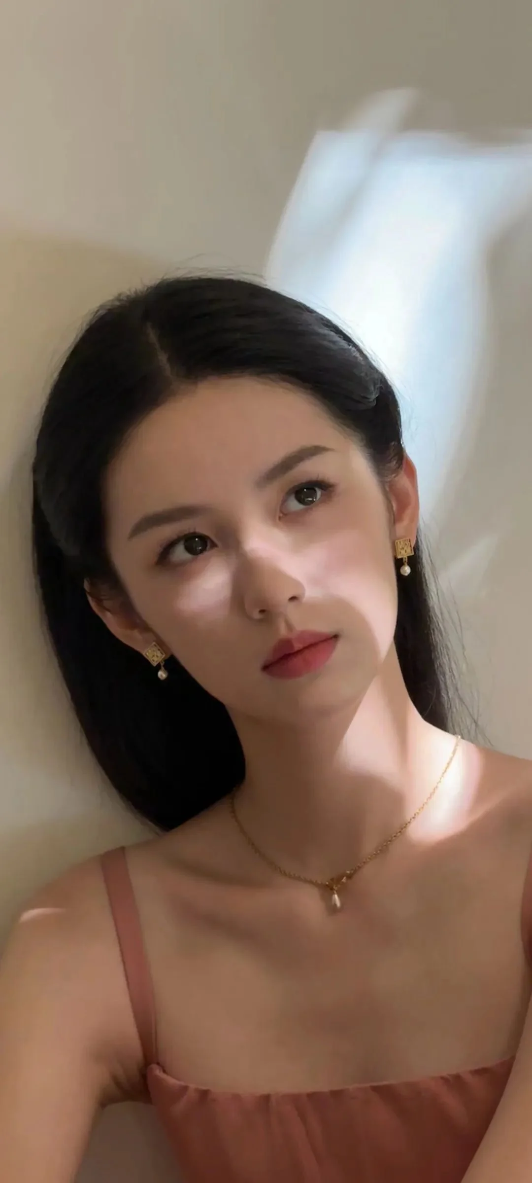 一名女性靠在室内墙边，在柔和光影下看向镜头。