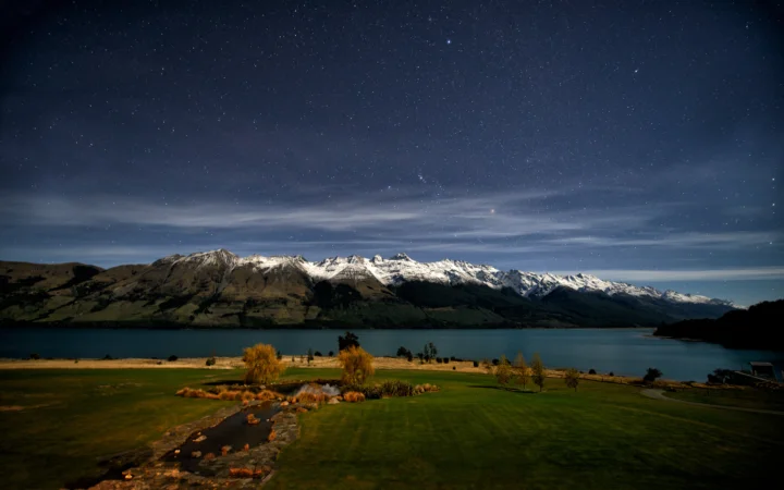 夜空下，积雪山脉、湖泊与草地构成宁静的自然景观。